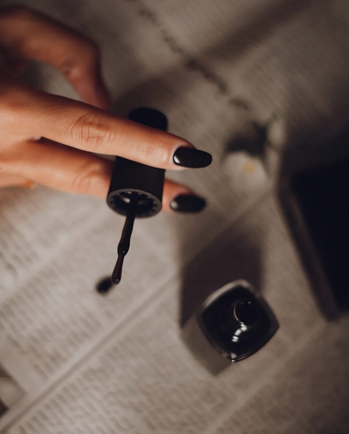 A hand holding a brush of black nail polish above the open bottle