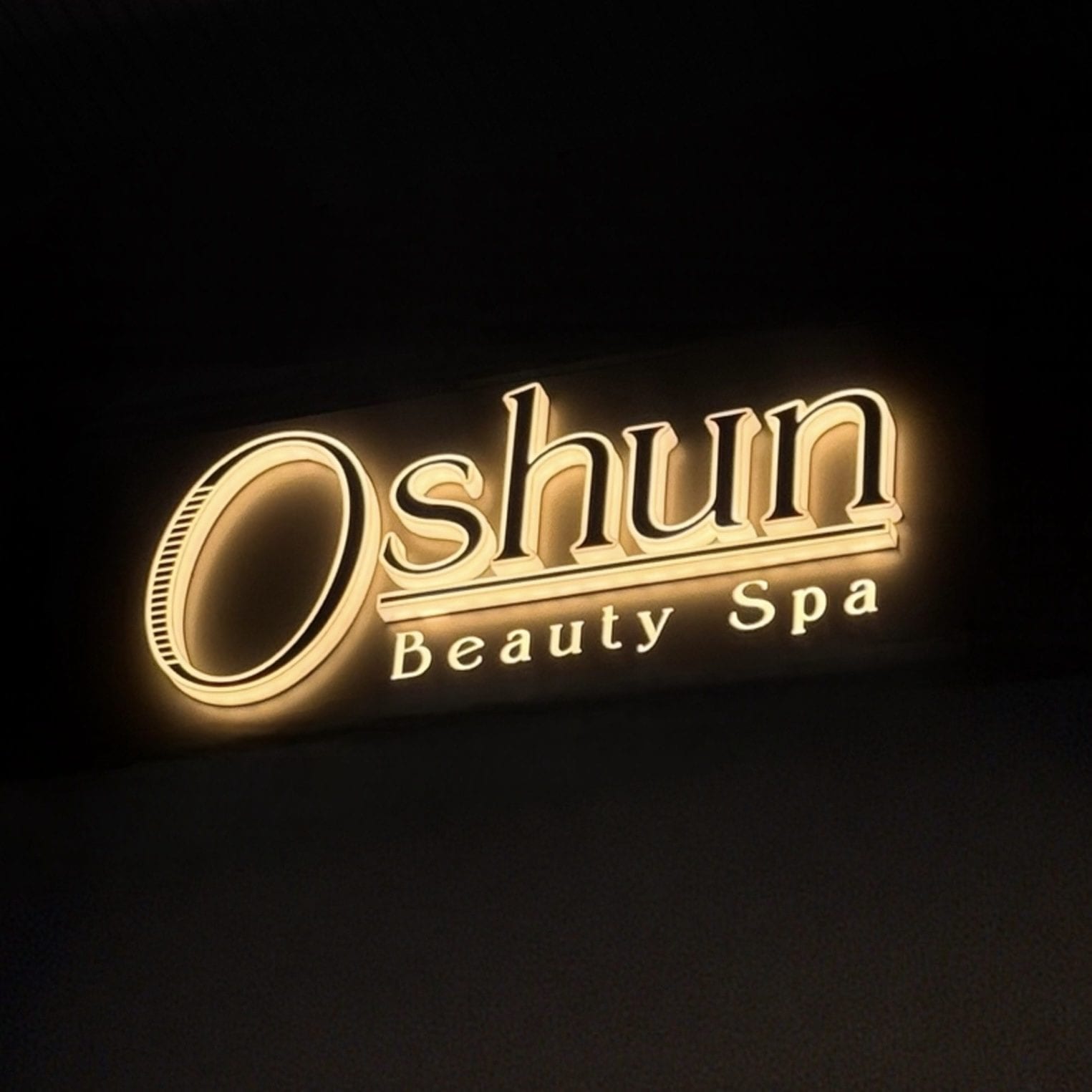 The illuminated Oshun Beauty Spa sign in champagne gold on black