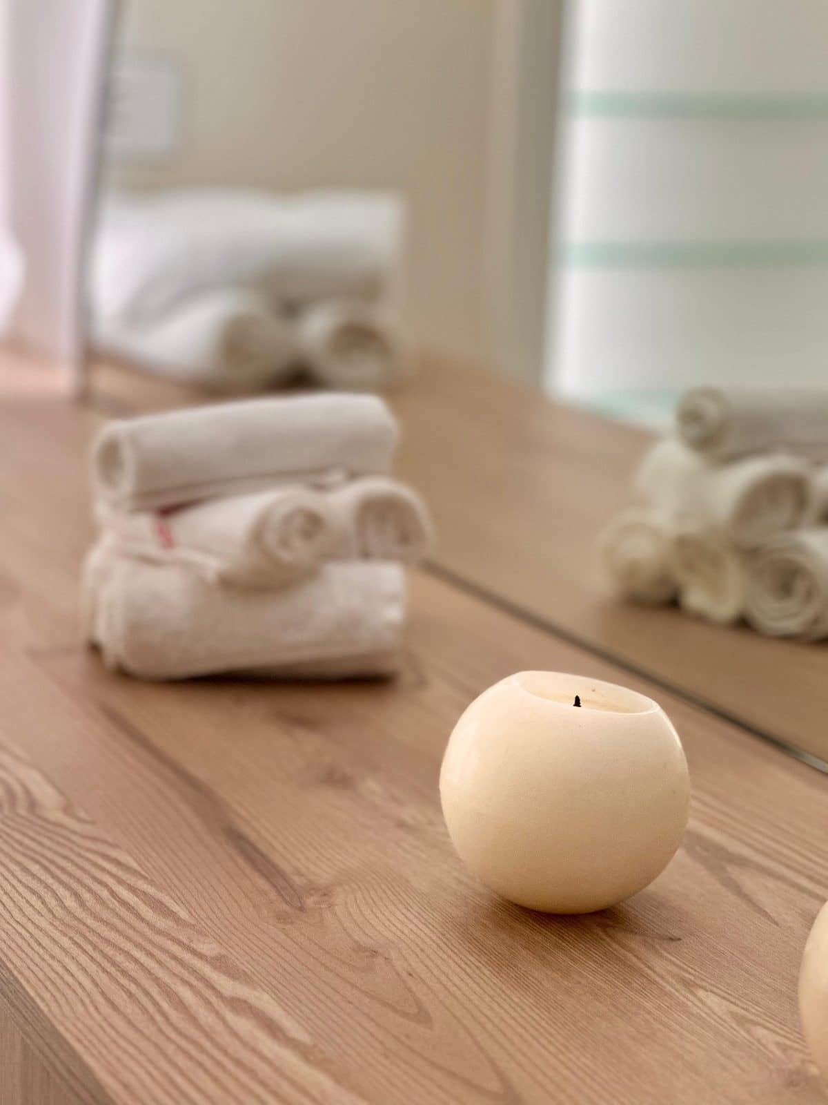 A round cream candle and folded towels on a wooden counter at Oshun Beauty Spa